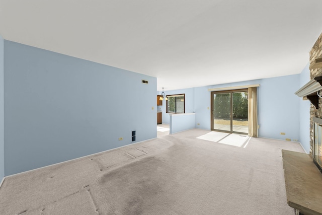 unfurnished living room featuring a stone fireplace, carpet, and a notable chandelier