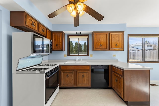 kitchen featuring black dishwasher, brown cabinetry, a peninsula, white gas stove, and a sink