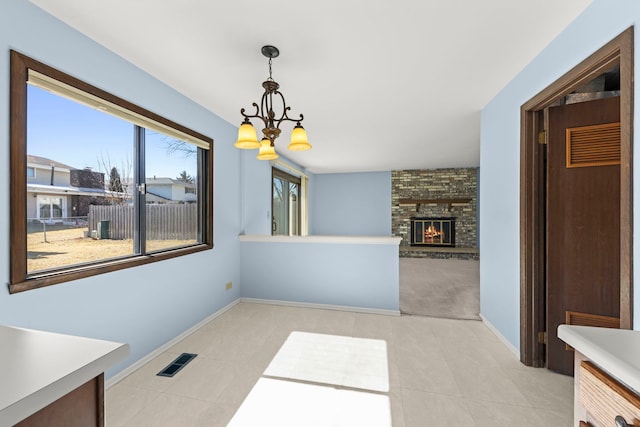 unfurnished dining area with a fireplace, light tile patterned floors, visible vents, an inviting chandelier, and baseboards