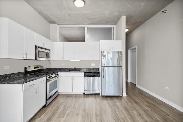 kitchen featuring sink, dark stone counters, stainless steel appliances, light hardwood / wood-style floors, and white cabinets