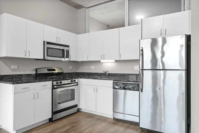 kitchen with sink, white cabinetry, dark stone countertops, appliances with stainless steel finishes, and dark hardwood / wood-style floors