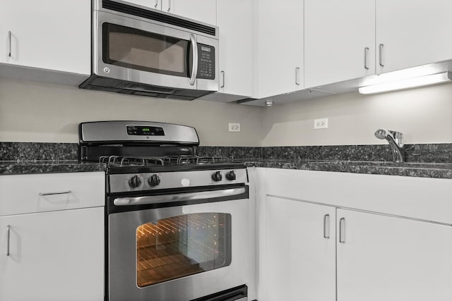 kitchen with stainless steel appliances, white cabinetry, sink, and dark stone countertops