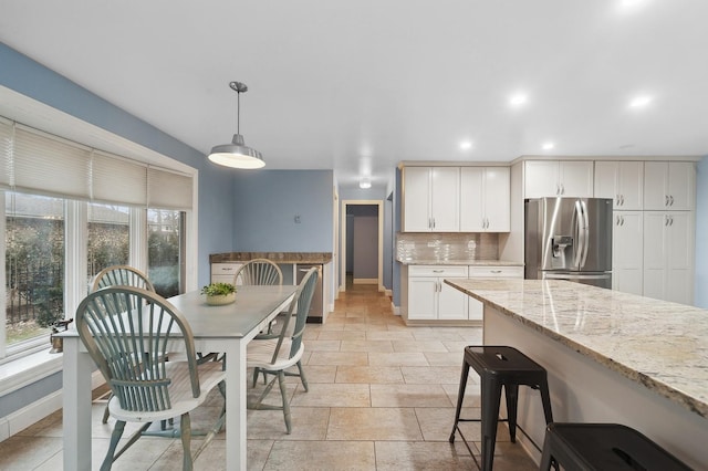 kitchen featuring white cabinetry, light stone counters, stainless steel fridge with ice dispenser, hanging light fixtures, and backsplash