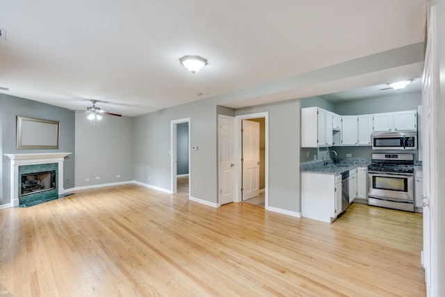 kitchen with sink, a premium fireplace, white cabinetry, stainless steel appliances, and light hardwood / wood-style floors