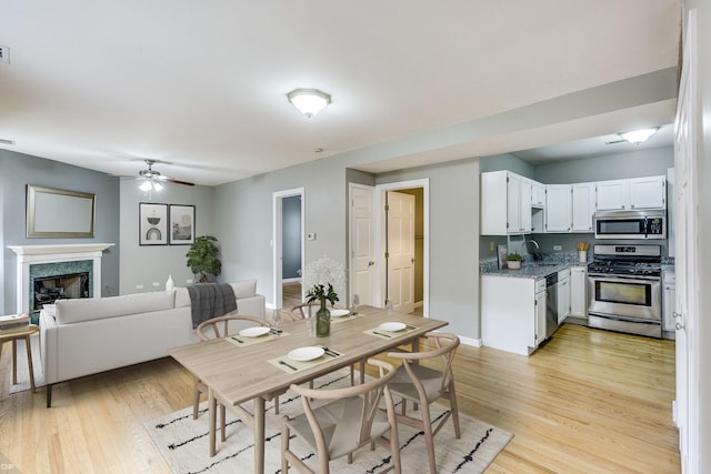 dining area with a premium fireplace, sink, ceiling fan, and light hardwood / wood-style flooring