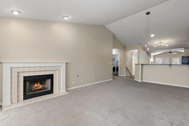 unfurnished living room featuring a tile fireplace, ceiling fan, independent washer and dryer, light carpet, and vaulted ceiling