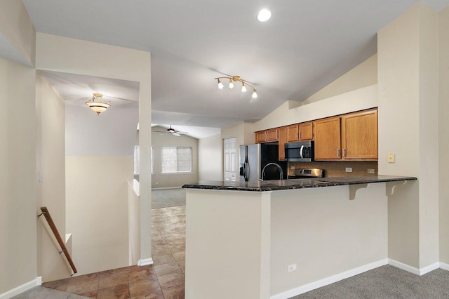 kitchen featuring lofted ceiling, dark stone countertops, ceiling fan, kitchen peninsula, and stainless steel appliances