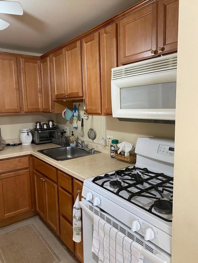 kitchen featuring brown cabinetry, white appliances, light countertops, and a sink