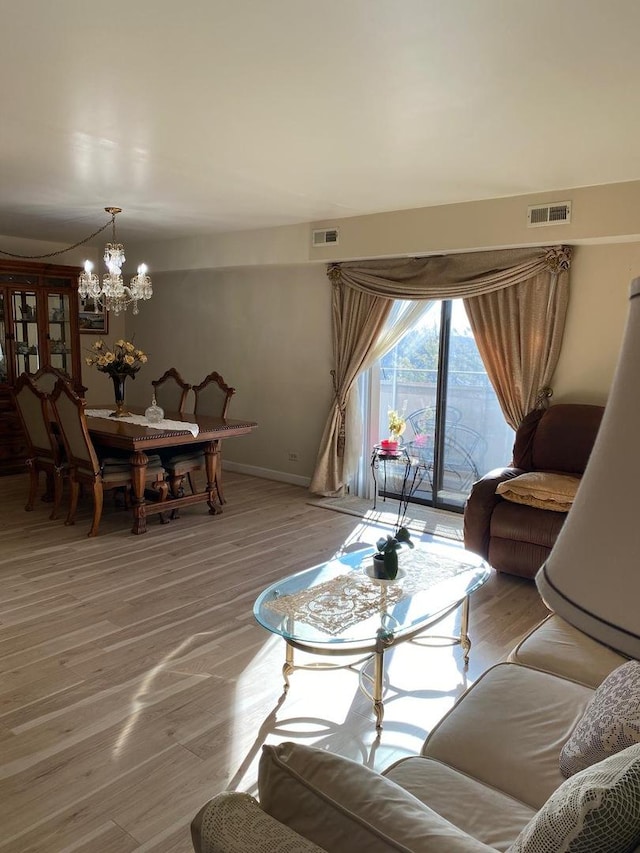 living room with baseboards, light wood-style flooring, visible vents, and an inviting chandelier