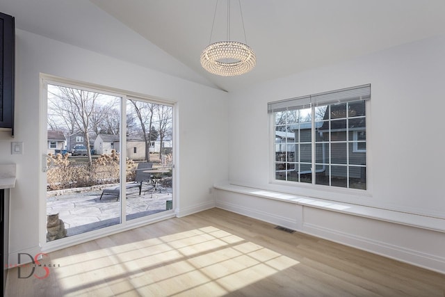 unfurnished dining area with a chandelier, vaulted ceiling, and hardwood / wood-style floors