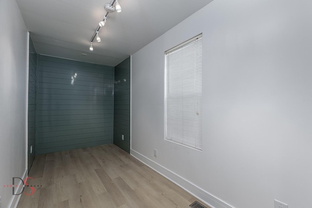 spare room with track lighting, light wood-type flooring, and wood walls