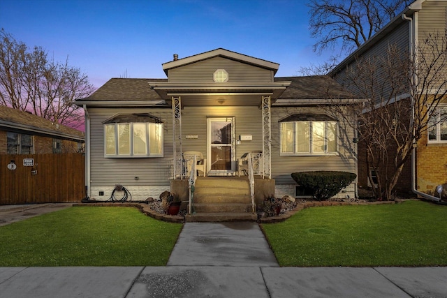 view of front facade featuring a shingled roof, a lawn, and fence