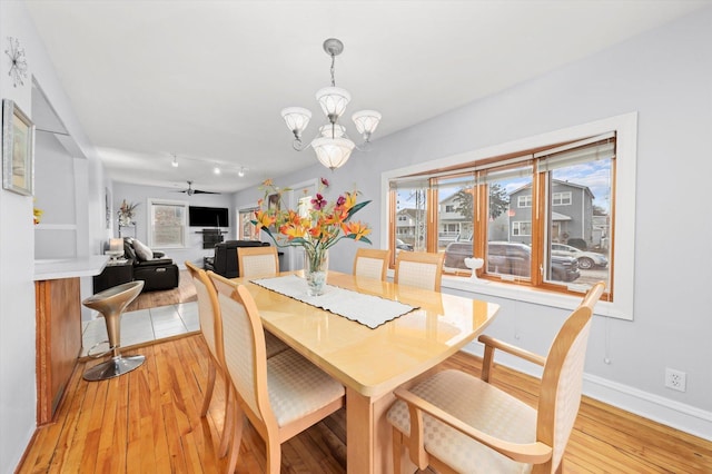 dining space featuring light wood finished floors, baseboards, and ceiling fan with notable chandelier