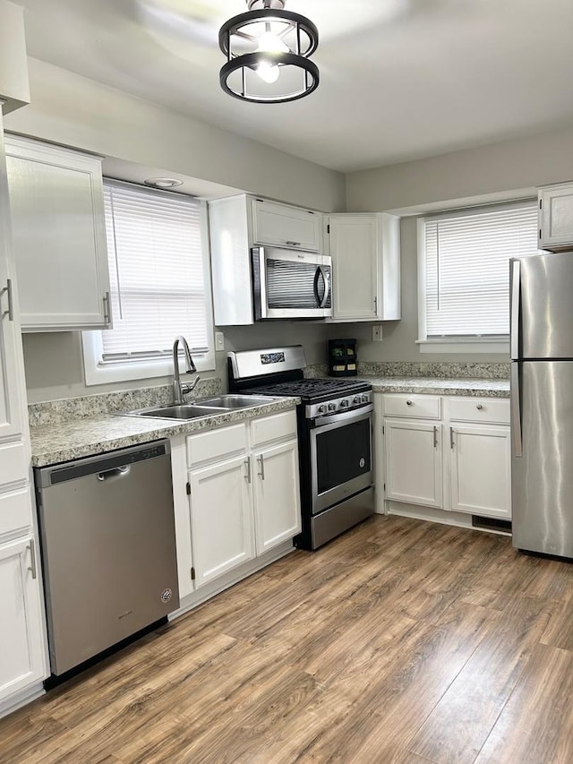 kitchen with appliances with stainless steel finishes, light hardwood / wood-style floors, sink, and white cabinets