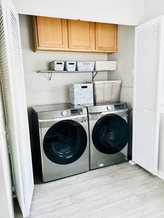 washroom featuring cabinets, light wood-type flooring, and washer and clothes dryer