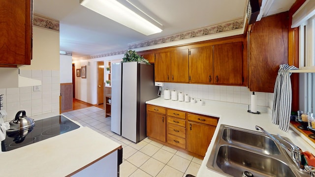 kitchen with sink, tasteful backsplash, light tile patterned floors, black electric cooktop, and stainless steel fridge