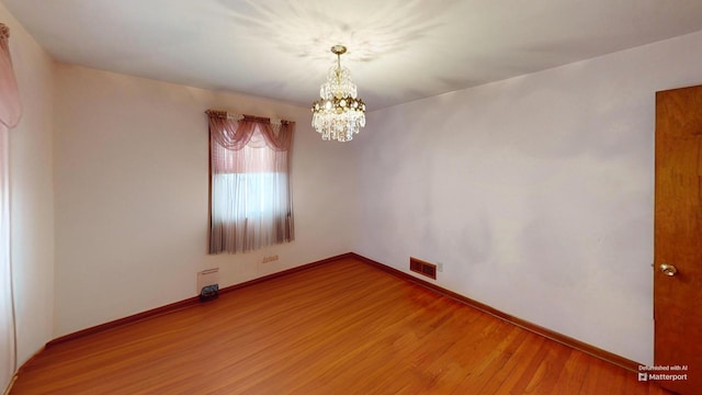 spare room featuring hardwood / wood-style flooring and a chandelier