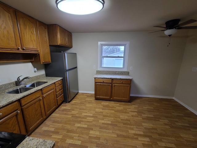 kitchen with sink, stainless steel fridge, ceiling fan, light stone countertops, and light wood-type flooring