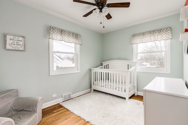 bedroom with ceiling fan, a nursery area, and light wood-type flooring