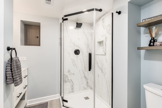 bathroom with hardwood / wood-style floors, a shower with shower door, vanity, electric panel, and toilet