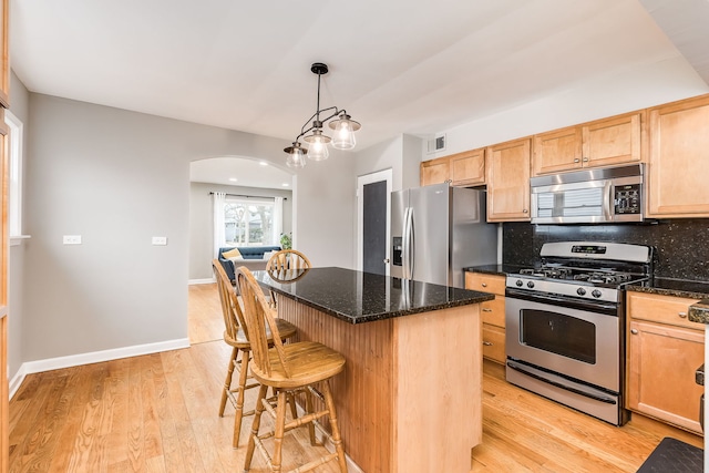 kitchen featuring a breakfast bar, dark stone countertops, hanging light fixtures, a center island, and stainless steel appliances