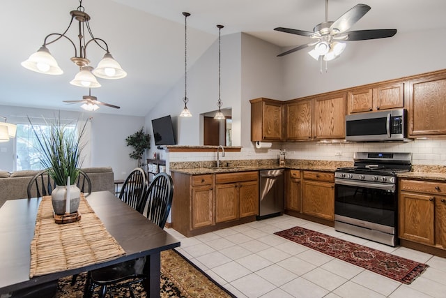 kitchen featuring sink, stone counters, appliances with stainless steel finishes, hanging light fixtures, and tasteful backsplash