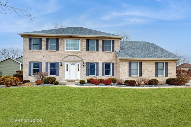 colonial house with brick siding, a front yard, and roof with shingles