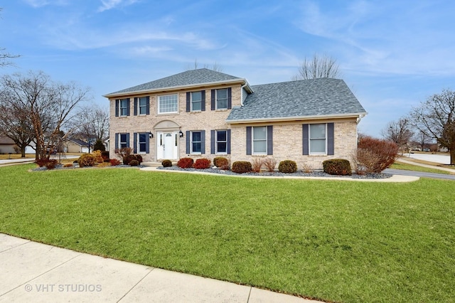 colonial house with a shingled roof, a front yard, and brick siding