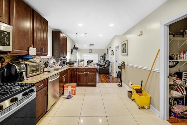 kitchen with light tile patterned flooring, sink, hanging light fixtures, kitchen peninsula, and stainless steel appliances