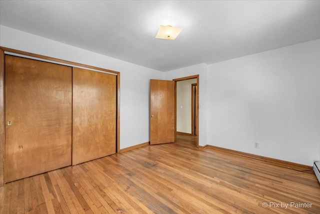 unfurnished bedroom featuring a closet, a baseboard radiator, hardwood / wood-style flooring, and baseboards