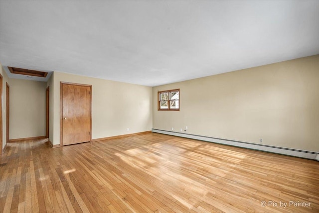 empty room with light wood-style floors, attic access, baseboards, and baseboard heating