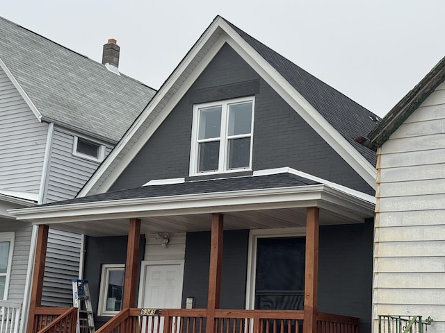 exterior space featuring brick siding, a porch, a chimney, and a shingled roof