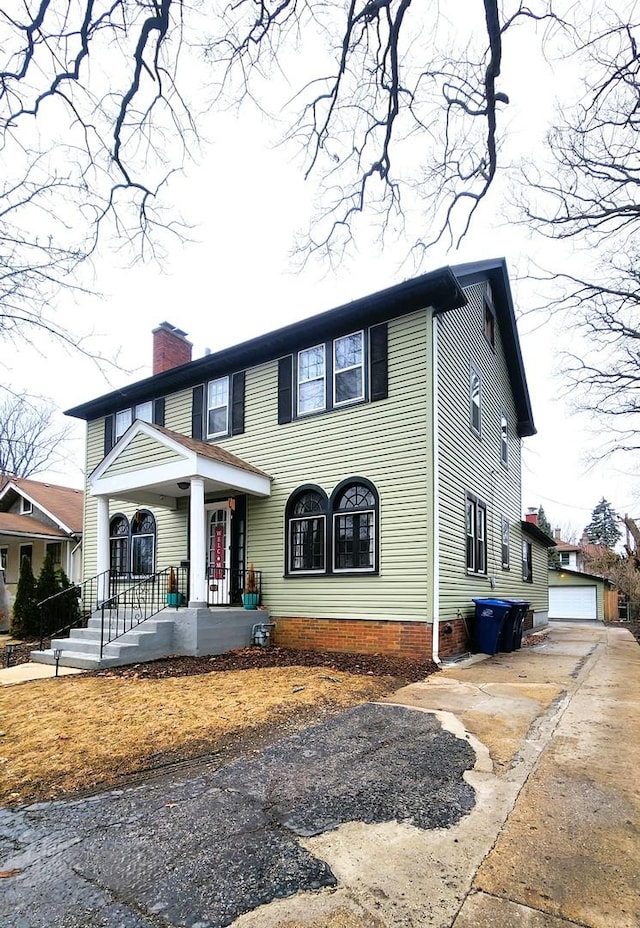 view of front of home with a garage, a porch, a chimney, and an outdoor structure