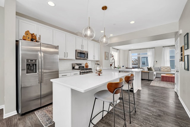 kitchen featuring backsplash, open floor plan, appliances with stainless steel finishes, a breakfast bar area, and dark wood-style flooring