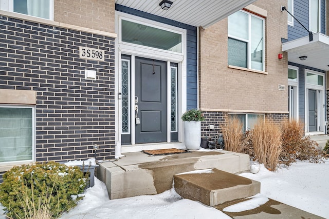 snow covered property entrance featuring brick siding