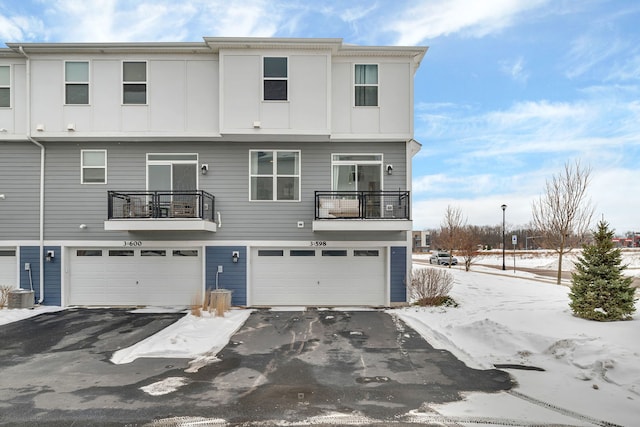 back of property featuring board and batten siding, aphalt driveway, central AC unit, a garage, and a balcony