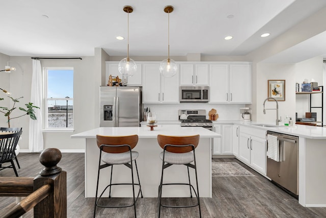 kitchen with a sink, backsplash, dark wood-style floors, appliances with stainless steel finishes, and light countertops