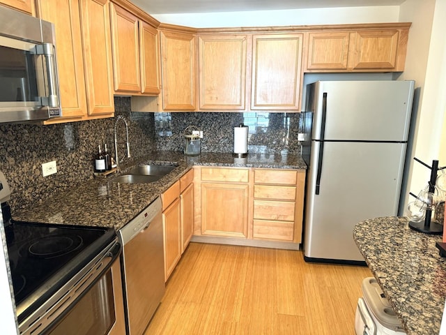 kitchen with sink, light hardwood / wood-style flooring, appliances with stainless steel finishes, backsplash, and dark stone counters