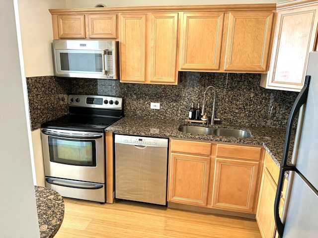 kitchen featuring sink, tasteful backsplash, dark stone counters, stainless steel appliances, and light hardwood / wood-style floors