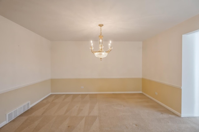 spare room featuring light colored carpet and a chandelier