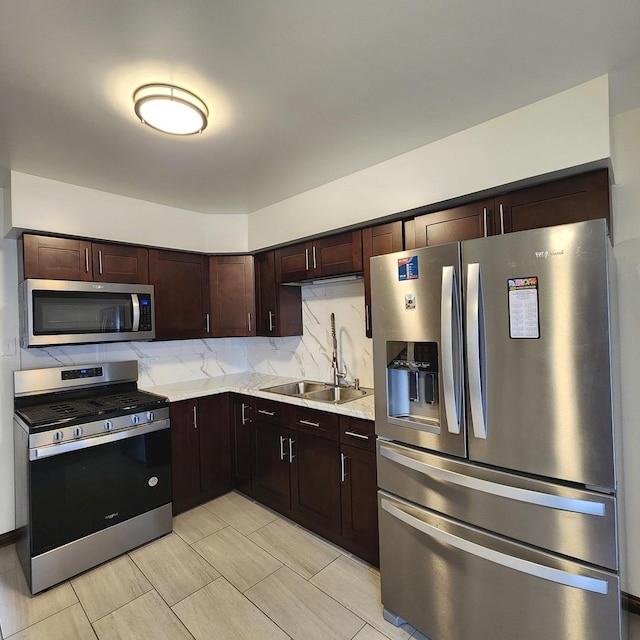 kitchen with appliances with stainless steel finishes, tasteful backsplash, sink, dark brown cabinetry, and light stone countertops