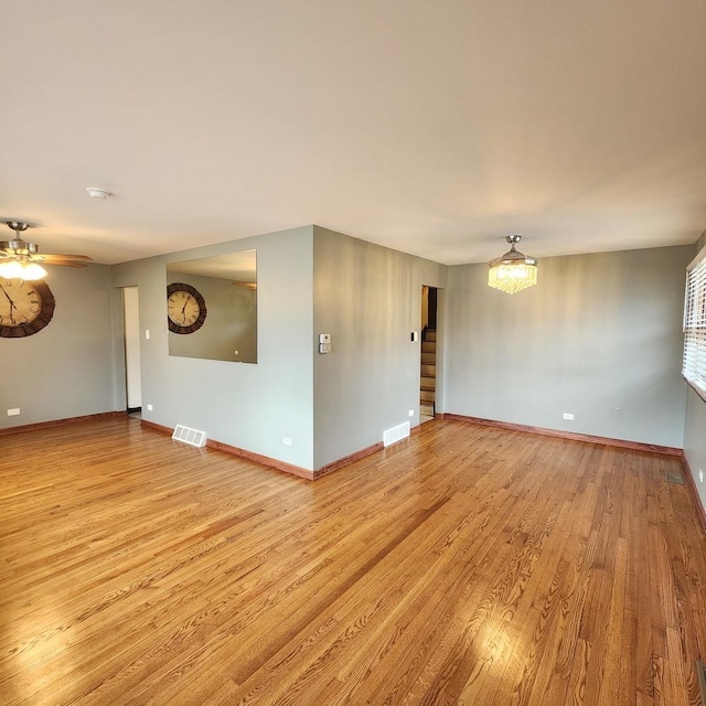 unfurnished room featuring ceiling fan with notable chandelier and light hardwood / wood-style flooring