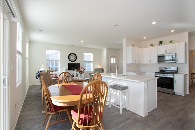 kitchen with dark wood-type flooring, sink, white cabinetry, a center island with sink, and stainless steel appliances