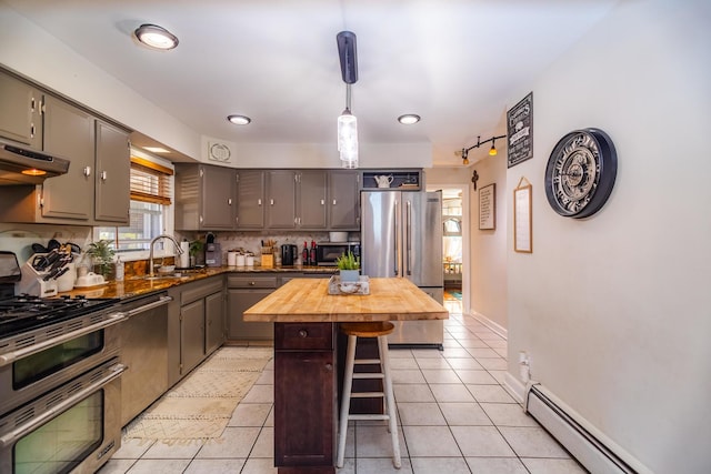 kitchen featuring pendant lighting, butcher block countertops, appliances with stainless steel finishes, a baseboard heating unit, and a kitchen island