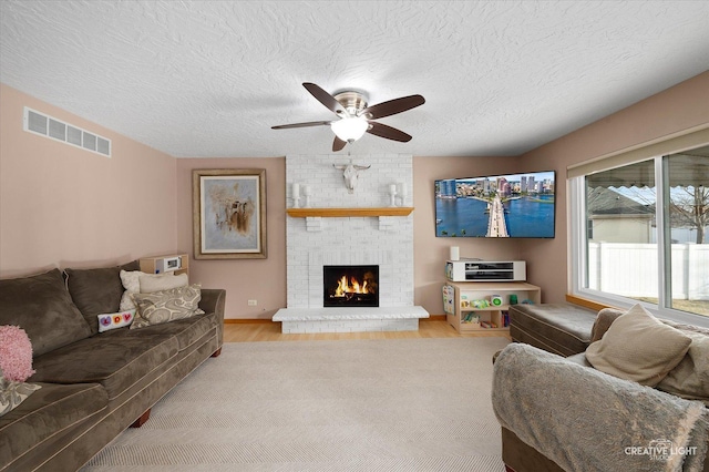 living room with ceiling fan, light hardwood / wood-style floors, a brick fireplace, and a textured ceiling