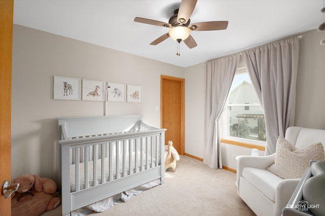 bedroom featuring a crib, light colored carpet, and ceiling fan