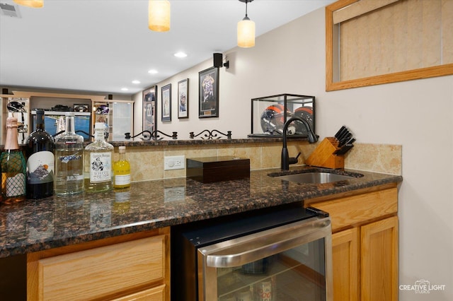 bar with sink, decorative light fixtures, beverage cooler, and dark stone counters