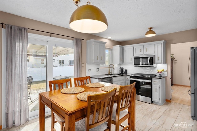 kitchen with sink, a textured ceiling, pendant lighting, stainless steel appliances, and backsplash