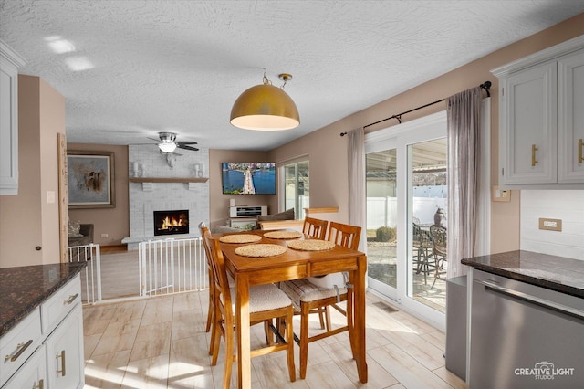 dining area with light hardwood / wood-style flooring, a textured ceiling, a fireplace, and ceiling fan