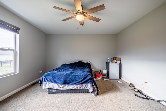 carpeted bedroom featuring multiple windows, stainless steel fridge, and ceiling fan